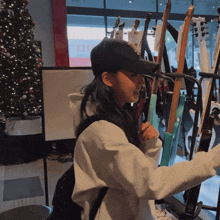 a woman in a baseball cap holds a guitar in front of a display of guitars