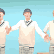three boys in school uniforms with their arms outstretched in front of a blue wall