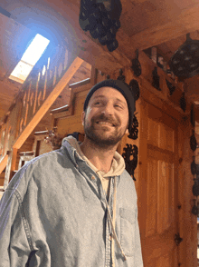 a man with a beard wearing a denim shirt and a beanie smiles
