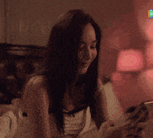 a woman sitting on a bed looking at her cell phone
