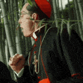 a man in a cardinal 's robe is standing in a bamboo forest .