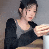 a woman wearing a black sweater and a gray tank top is sitting at a table