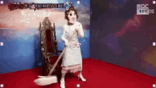 a woman in a white dress is standing in front of a chair with a mop in her hand