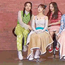 a group of young women are sitting on stools in front of a brick wall .