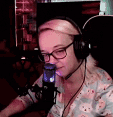 a woman wearing headphones and glasses is sitting in front of a microphone in a dark room .