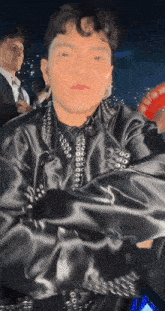 a man in a black jacket is standing with his arms crossed in a dark room .