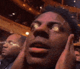 a close up of a man 's face with his hands on his ears in a theater .