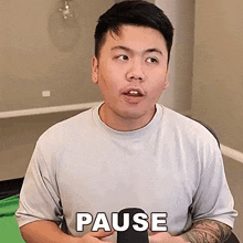 a man with a tattoo on his arm is holding a cell phone and making a pause gesture .