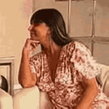 a woman in a pink dress is sitting on a couch with her hand to her mouth .