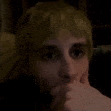 a person with blonde hair is covering their mouth with their hand