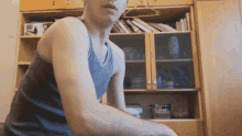 a man in a tank top stands in front of a bookcase