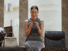 a woman in a grey dress is sitting at a table looking at her phone