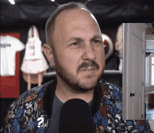 a man with a beard is talking into a microphone with a question mark on his neck