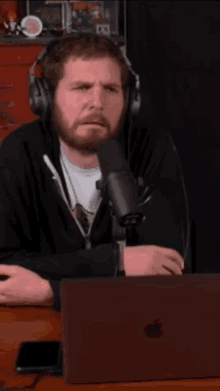 a man wearing headphones is singing into a microphone while sitting in front of an apple laptop