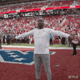 a man wearing headphones stands on a football field with his arms outstretched in front of a us bank banner