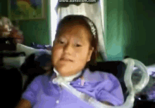 a girl in a purple shirt is sitting in a chair with an oxygen mask around her neck