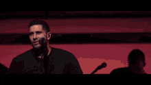 a man singing into a microphone in front of a red background