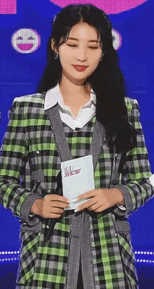 a woman in a green and gray plaid jacket is holding a microphone and a clipboard .
