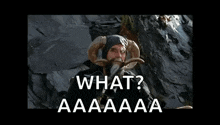 a man with a beard and horns is standing in front of a rock wall and says `` what ? aaaaaa '' .