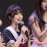 a girl is holding a microphone and smiling while standing next to another girl .