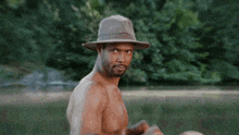 a shirtless man wearing a hat is standing in front of trees and a sign that says " i love you "