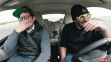 two men are laughing in a car with the word thinki jules on the steering wheel