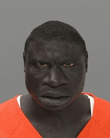 a man with a black face is wearing an orange shirt and looking at the camera