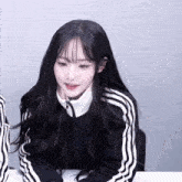 a girl with long black hair wearing a black adidas jacket