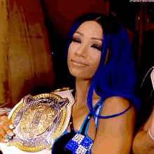 a woman with blue hair is holding a gold and silver championship belt