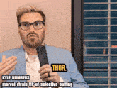 a man in a suit and glasses holds a microphone and says kyle numbers