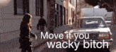 a woman walking down a street next to a car that says move it you wacky bitch ..