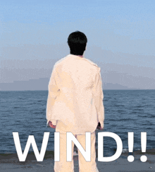a man in a white shirt is standing on a beach with the word wind written in white