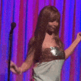 a woman is dancing on a stage in front of a purple curtain with her hair blowing in the wind .