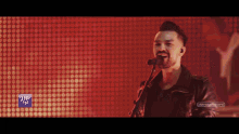 a man singing into a microphone with a blue sign that says ' aer gaz ' on it