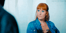 a woman with red hair and blue eyes wearing a denim jacket