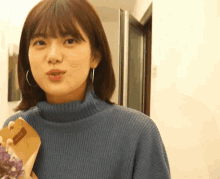 a woman wearing a blue sweater is holding a bouquet of flowers .