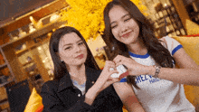 two girls are making a heart shape with their hands and one has a shirt that says helly paris