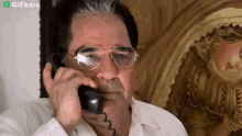 a man wearing glasses is talking on a phone with a gifkaro watermark