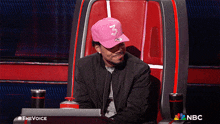 a man wearing a pink hat with the number 3 on it sits in a nbc chair