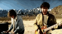 a man is playing a keyboard while another man plays a guitar