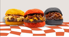 three different colored hamburgers are sitting on a checkered tablecloth