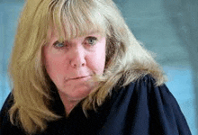 a woman with blonde hair and blue eyes is wearing a black robe and making a serious face .