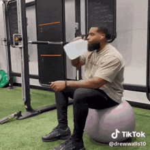 a man is drinking water while sitting on a ball with a tiktok watermark