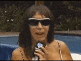 a woman wearing sunglasses is holding a microphone and talking into it .