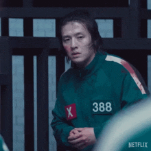 a man in a green jacket with a red x on his chest is standing in front of a fence .