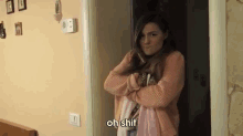 a woman in a pink sweater is standing in a doorway with her arms crossed and says oh shit .