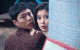 a man and a woman are peeking out from behind a blue tiled wall
