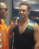 a man in a black tank top is being interviewed by a man in an orange shirt .