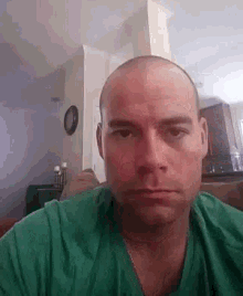 a bald man in a green shirt is sitting on a couch looking at the camera .