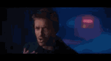 a man is singing into a microphone in a dark room in front of a red light .